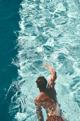 A focused triathlete swimming powerfully through clear blue water under bright sunlight.