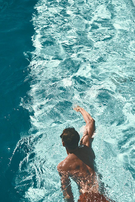 A vibrant photo of swimmers diving into a sparkling pool under a clear blue sky.