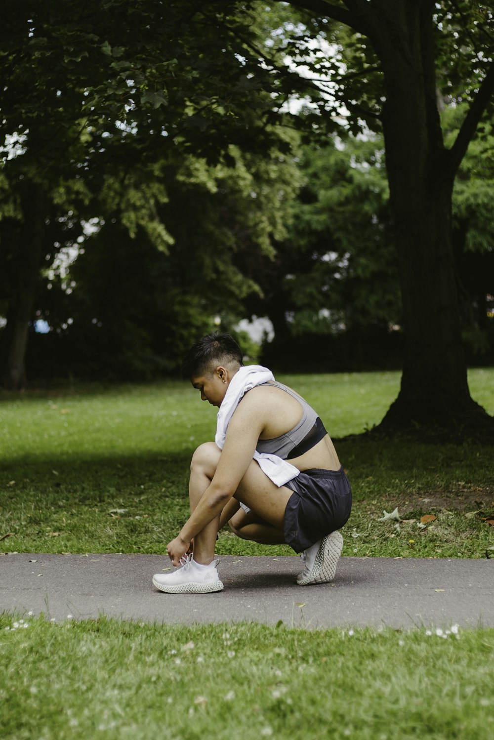 a woman squatting down on a sidewalk in a park