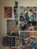 A collection of vintage posters is displayed on a wall, including a mix of music and artistic themes. One poster features a stylized graphic design with abstract shapes, while another depicts a person wearing a striped shirt. There are several concert posters, one of which advertises a performance by Dee Dee Ramone, showcasing a musician with a guitar. Another poster features an artistic depiction of a diver against a scenic backdrop. The overall aesthetic includes bold typography and graphics typical of counter-culture or punk music scenes.