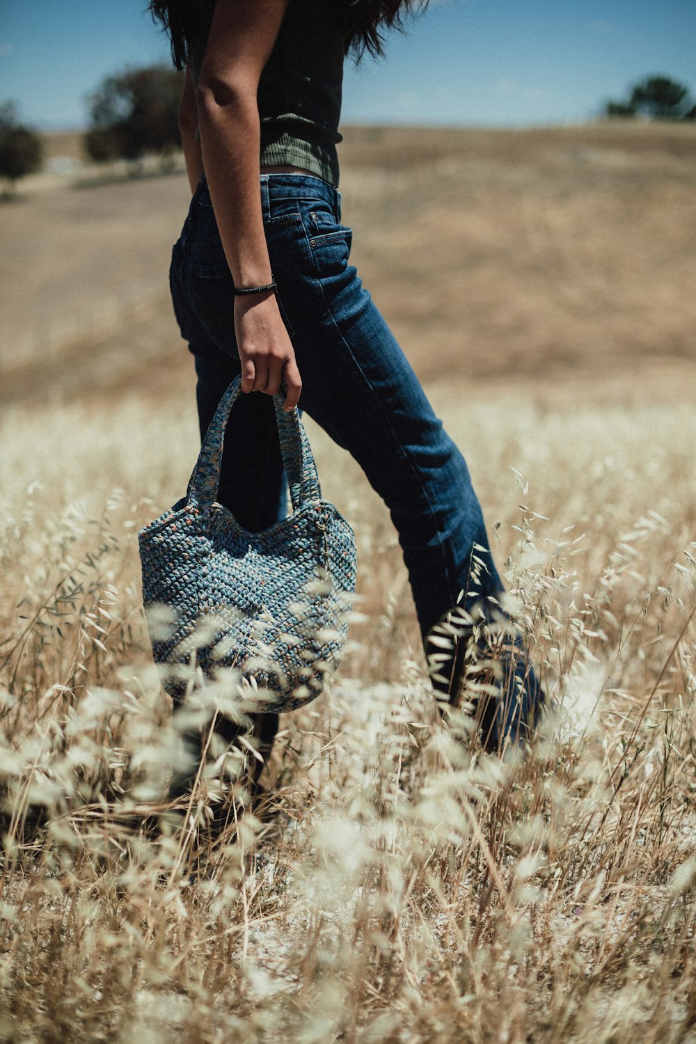 a woman walking through a field carrying a purse