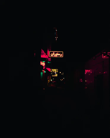 Silhouetted figures gathered around a glowing red neon sign in a dark alleyway.