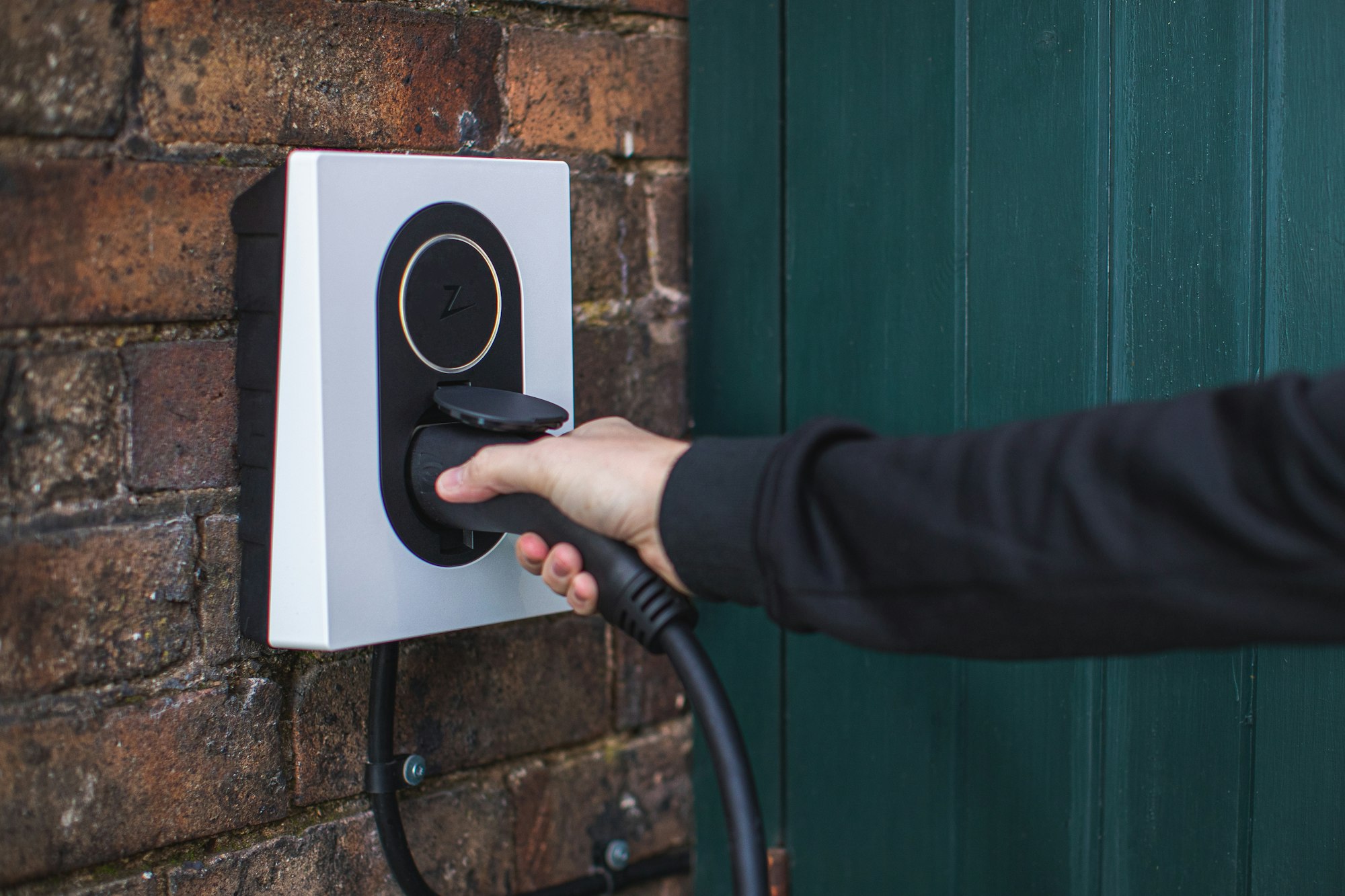 Owner taking out plug from an electric car charger mounted on wall