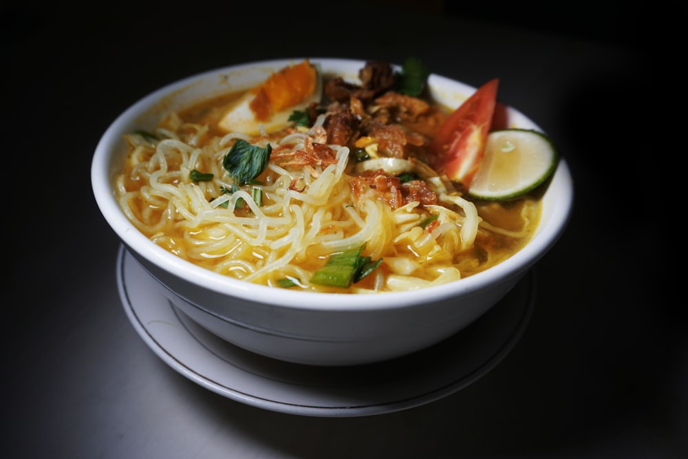 a white bowl filled with noodles, meat and vegetables