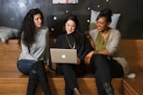 three women sitting on a bench looking at a laptop