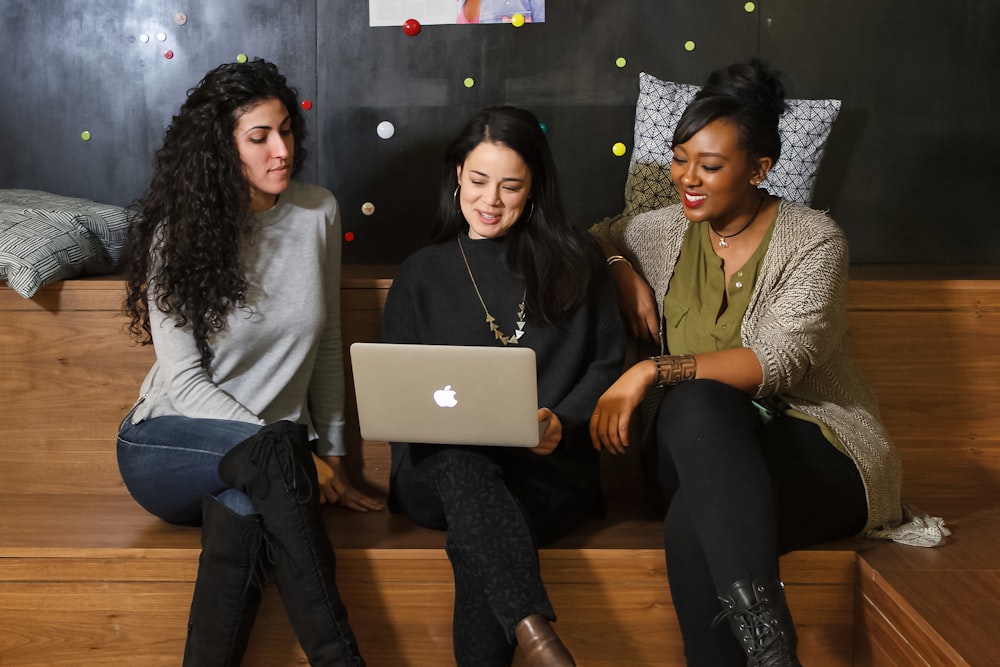 three women sitting on a bench looking at a laptop