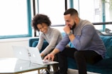 a man and woman sitting on a couch looking at a laptop