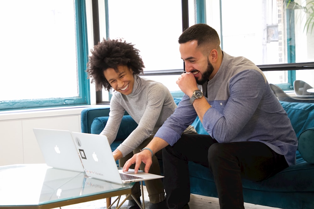 a man and woman sitting on a couch looking at a laptop