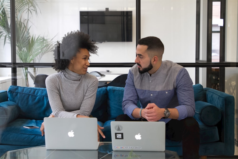 a man and a woman sitting on a couch with laptops