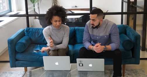 a man and woman sitting on a couch with their laptops