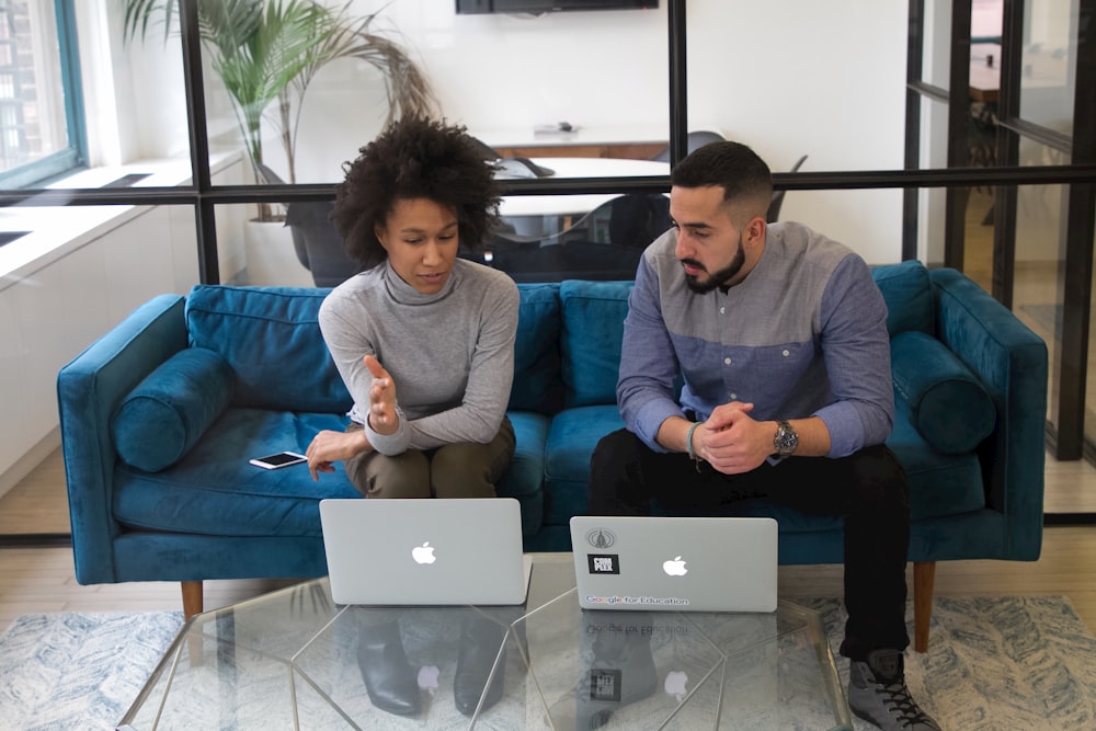 a man and woman sitting on a couch with their laptops