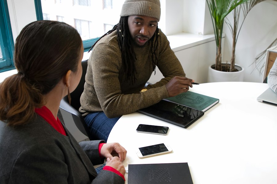 Two people discussing work at a table with a notebook