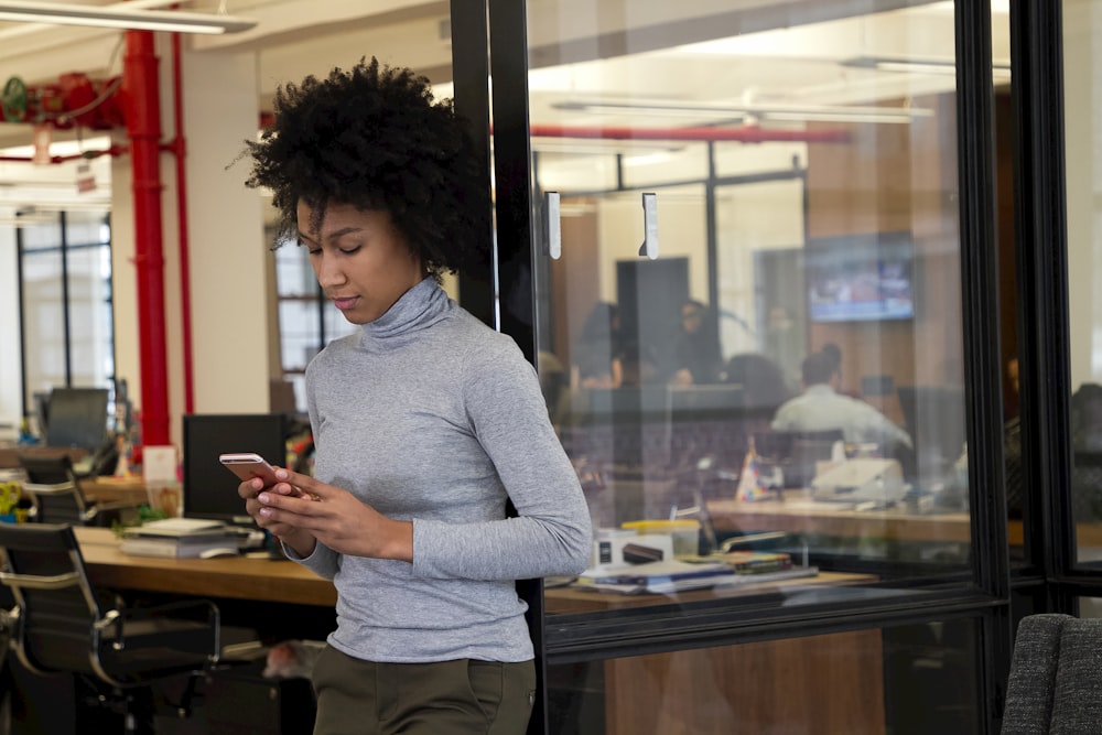 a woman standing in an office looking at her cell phone