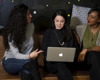 three women sitting on a bench looking at a laptop