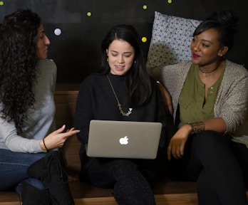Drei Damen unterhalten sich nett und sehen sich auf einem Apple MacBook das all in one Business an