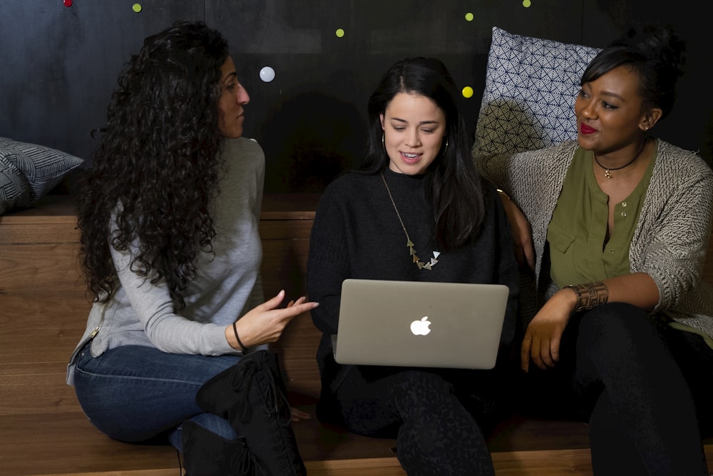 three women sitting on a bench looking at a laptop