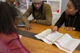 a man and woman sitting at a table with an open book