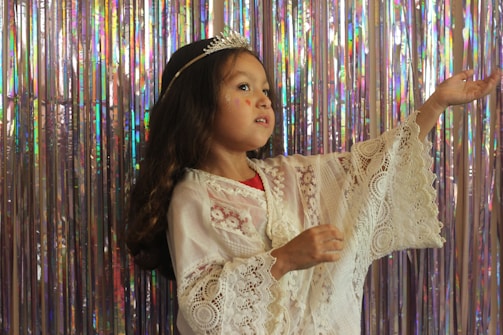 A close-up photo of Maitê wearing a tiny golden crown and a lilac dress, smiling softly.