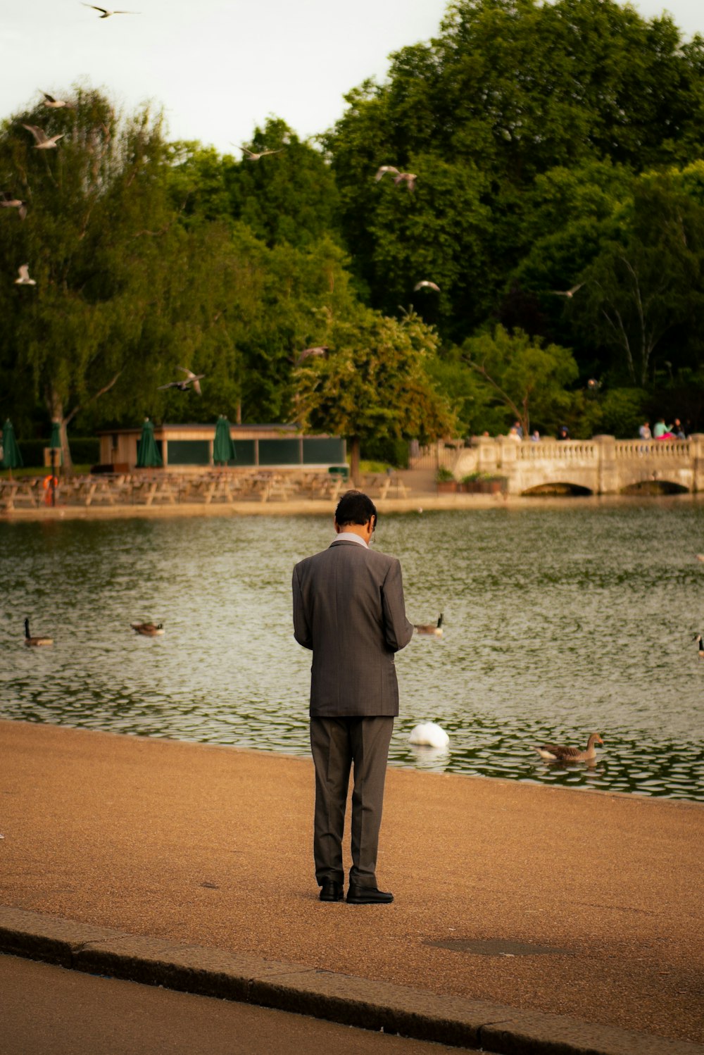 a man in a suit standing on the edge of a lake
