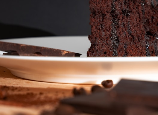 A close-up of a single slice of chocolate cake with a small scoop of vanilla ice cream on a white plate, bathed in natural daylight with soft shadows and a clean, minimal background.