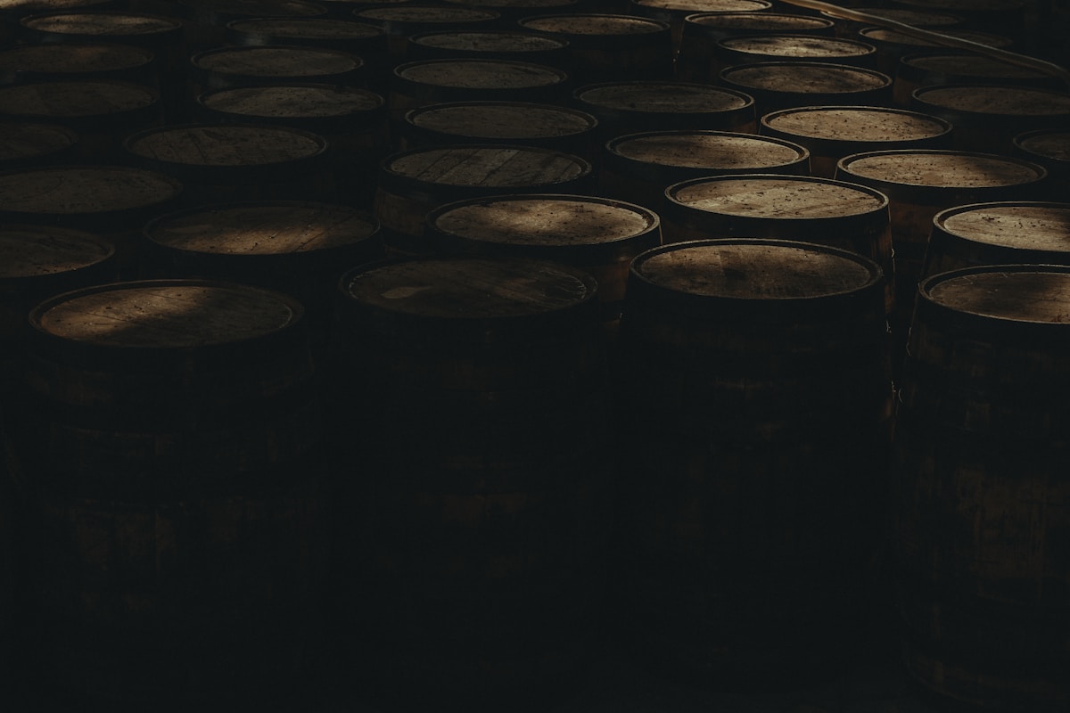 Whisky barrels in deep shadow, amber light, aged patina