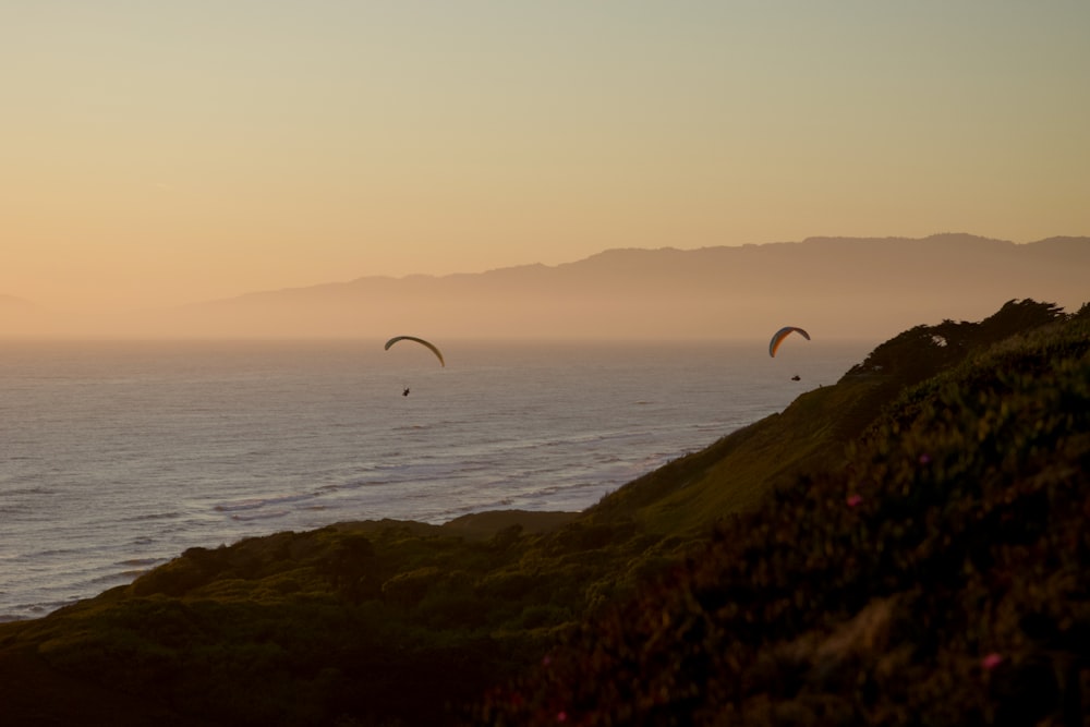Un couple de parapentes survolant l’océan au coucher du soleil