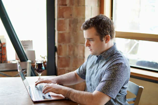 A cozy workspace with a laptop, running shoes, and a glass of red wine on a wooden table.