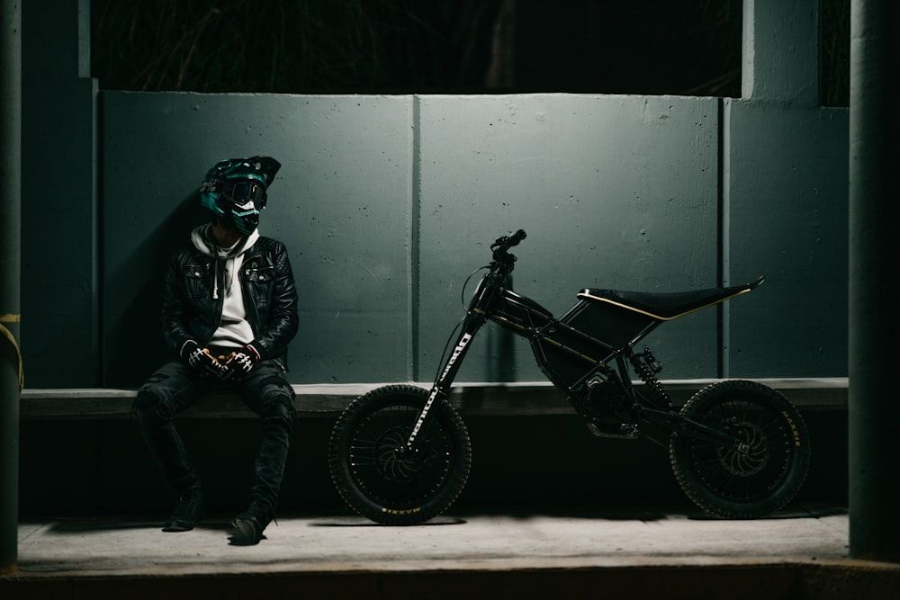 um homem sentado em uma saliência ao lado de uma bicicleta de terra