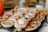 A close-up of a tray filled with an assortment of small pastries and savory tarts, some topped with whipped cream or garnished with herbs. Various textures and shapes are visible, including flaky crusts and creamy fillings, suggesting a variety of flavors.