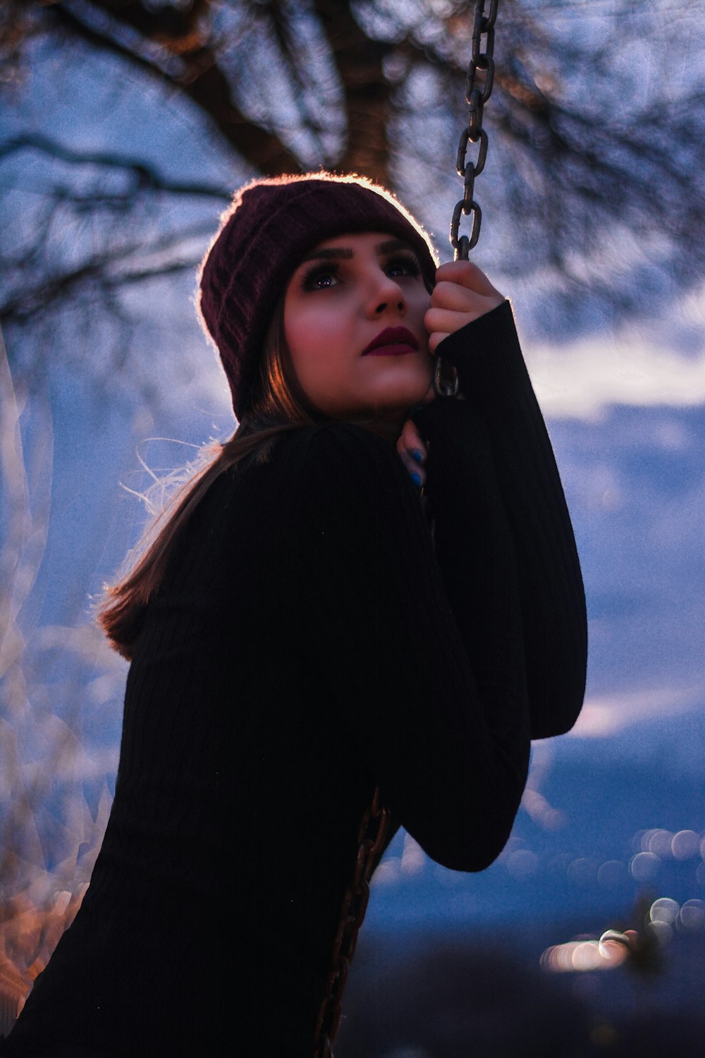 a woman is sitting on a swing with a hat on