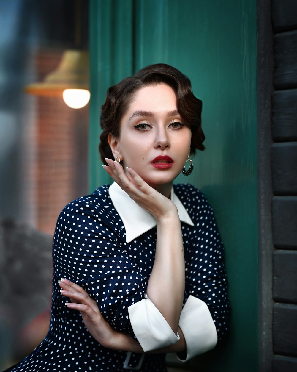 a woman leaning against a wall with her hand on her chin