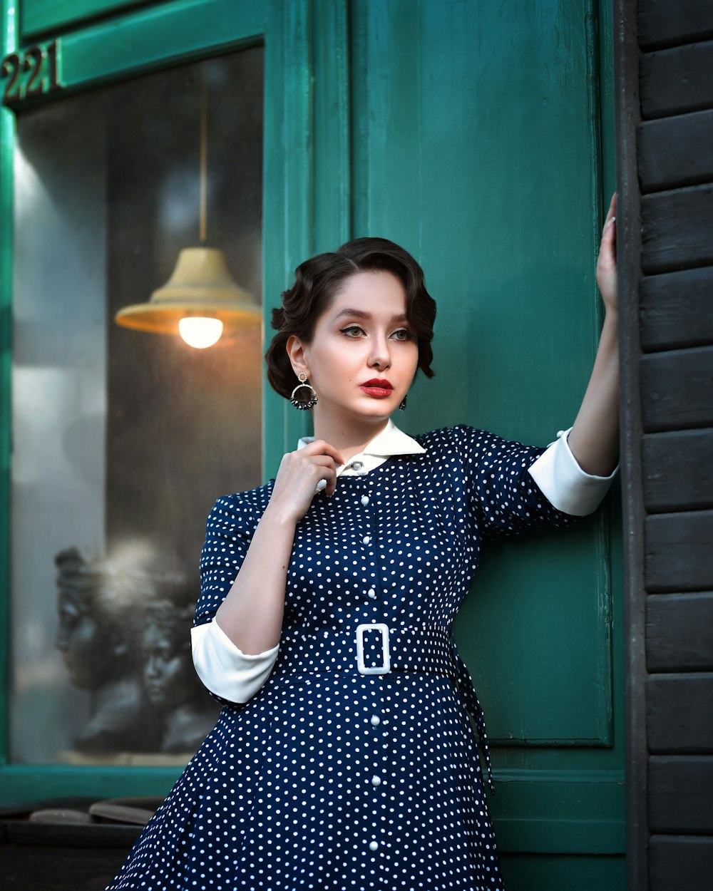 a woman in a blue dress leaning against a green door