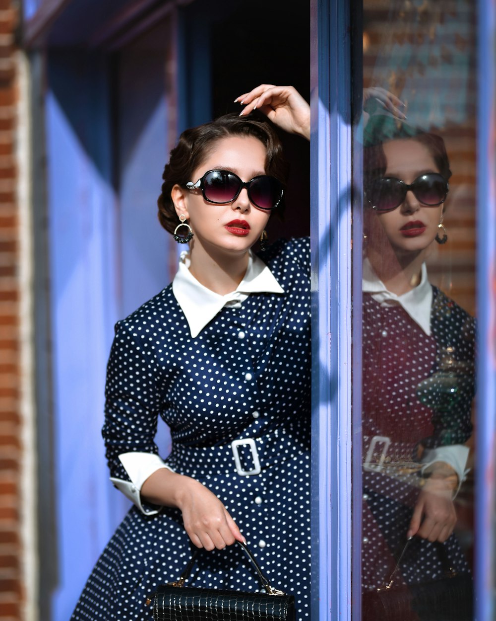 a woman in a dress and sunglasses leaning against a window