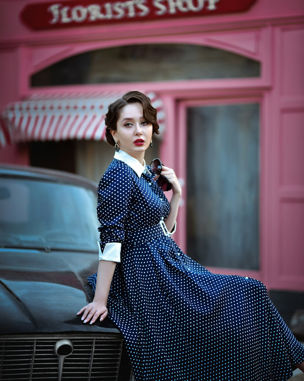 a woman in a polka dot dress leaning on a car