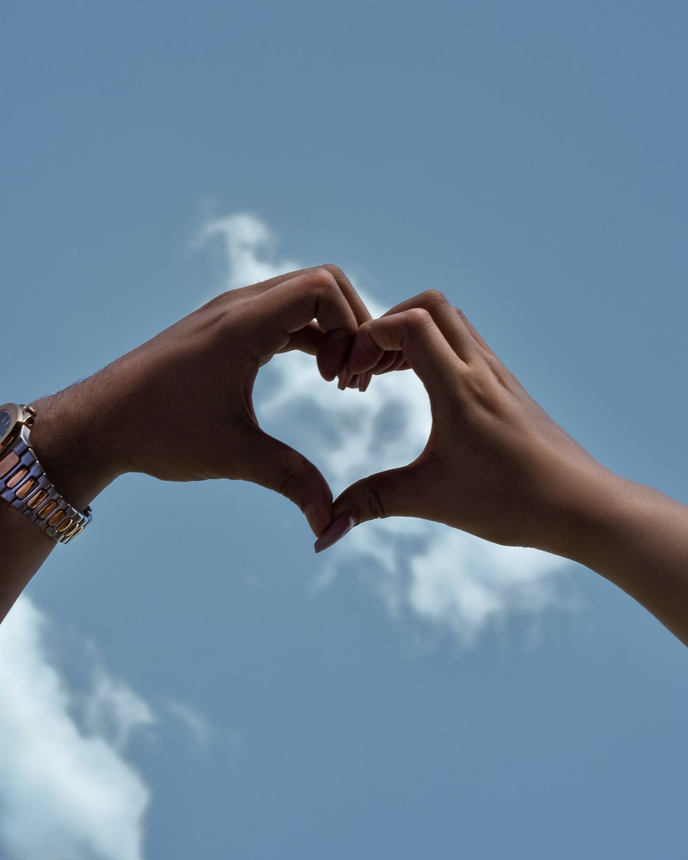 two hands making a heart shape against a blue sky