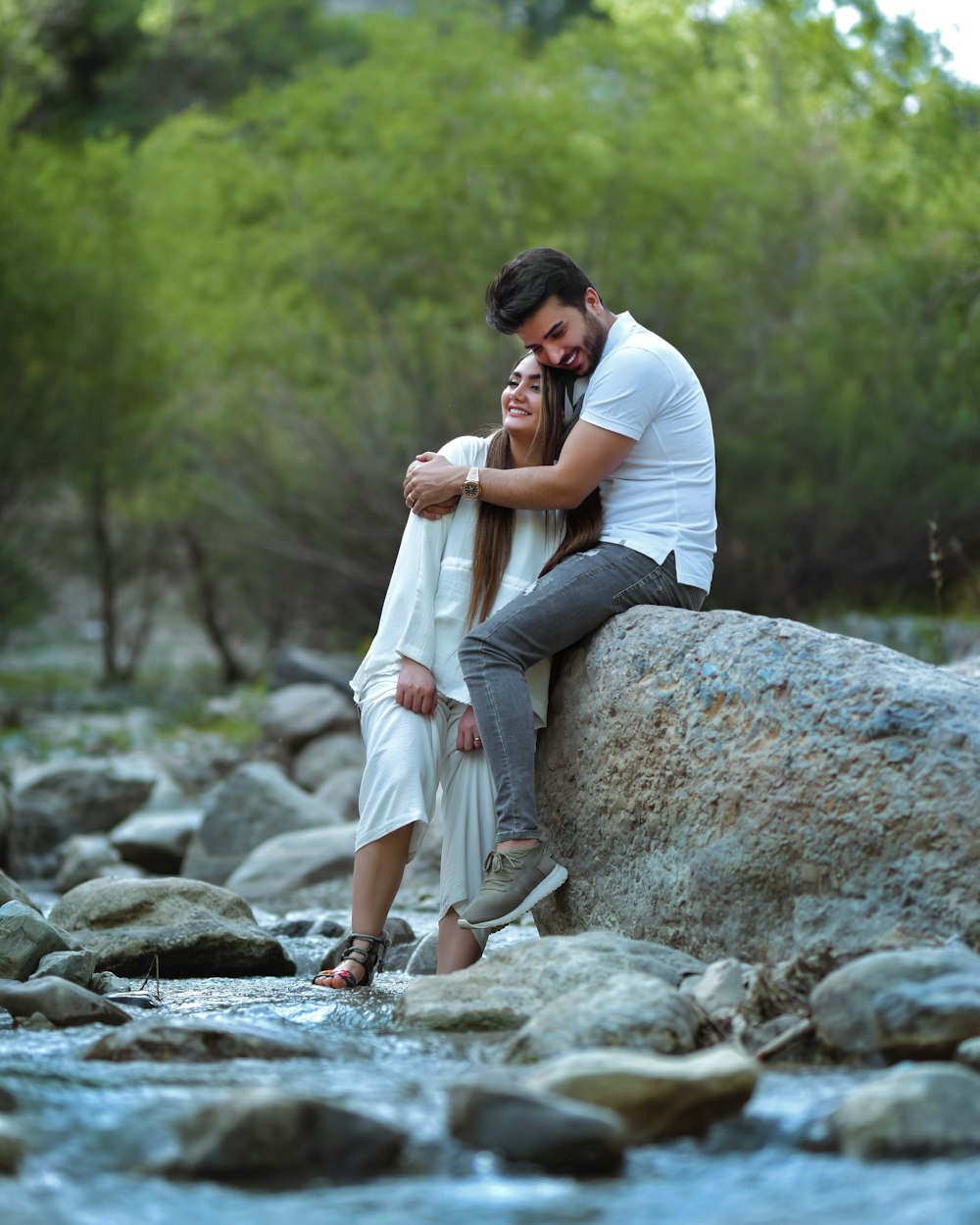 a man and a woman sitting on a rock by a river