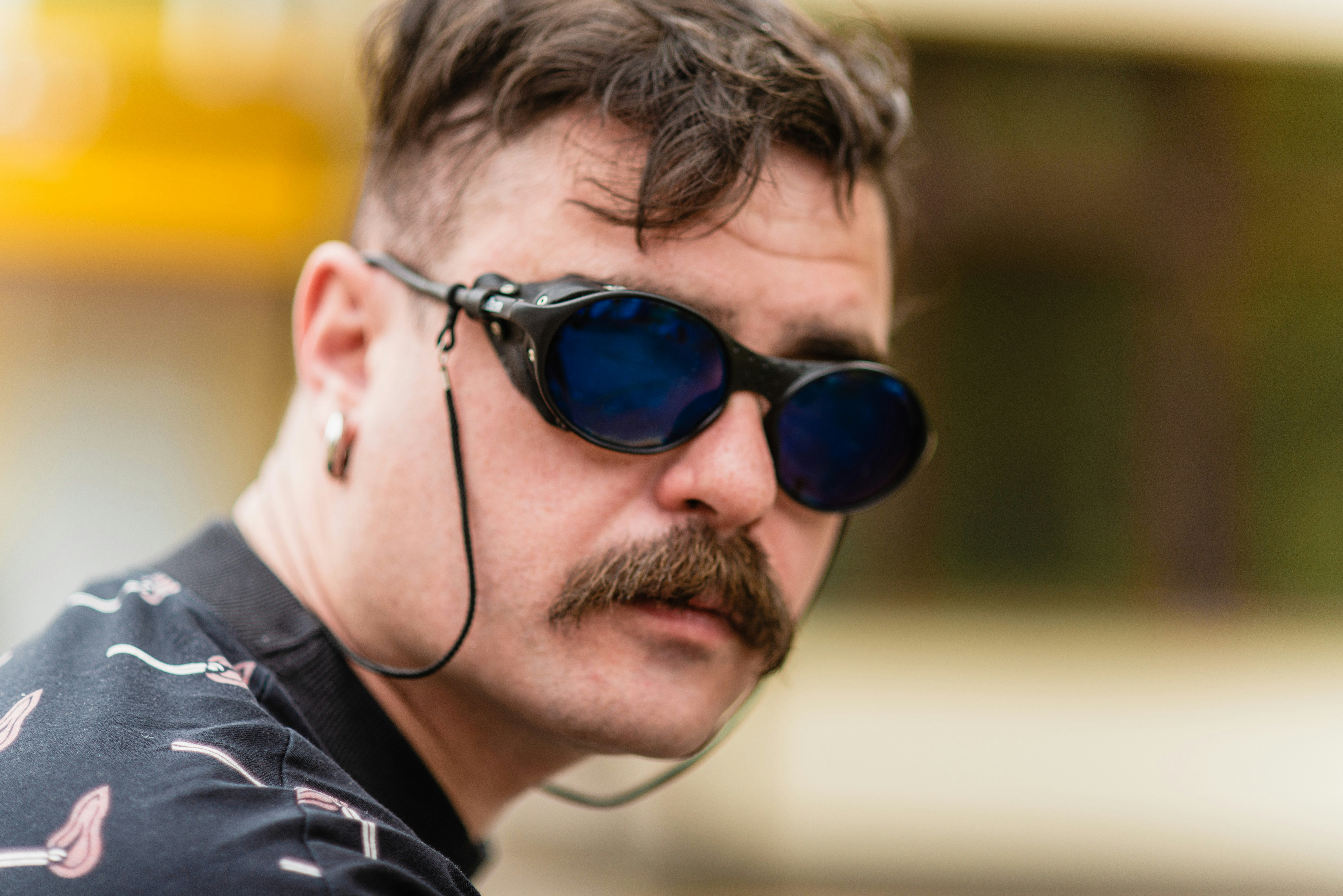 A man with a moustache wearing sunglasses and a pair of headphones