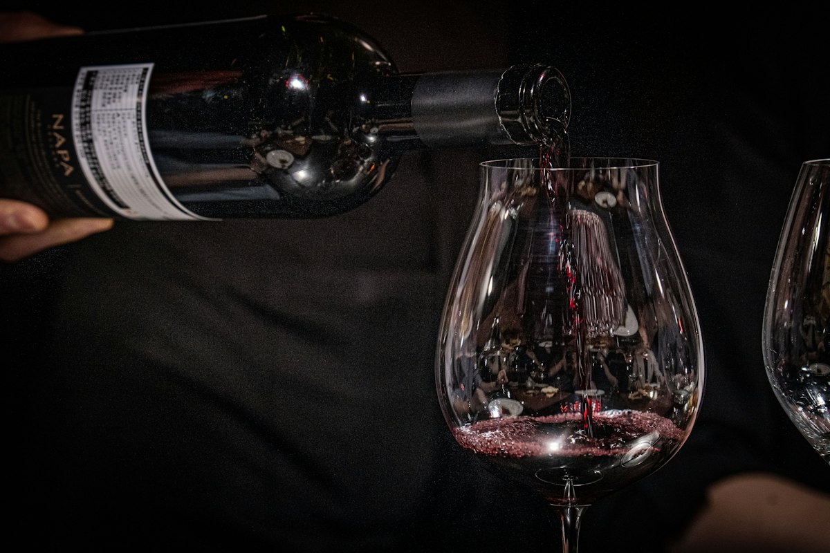 Red wine being poured from a dark bottle into a stemmed wine glass