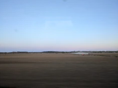 A sprawling field with fertilizer trucks unloading materials under a clear blue sky.