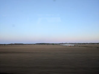 A panoramic drone shot capturing vast green farmland with tractors working under a clear blue sky.