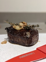 Close-up of a perfectly cooked steak on a wooden cutting board, garnished with fresh herbs.
