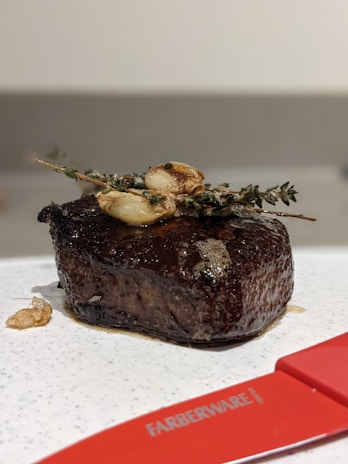 A close-up of a perfectly seared steak topped with fresh herbs on a rustic wooden plate.