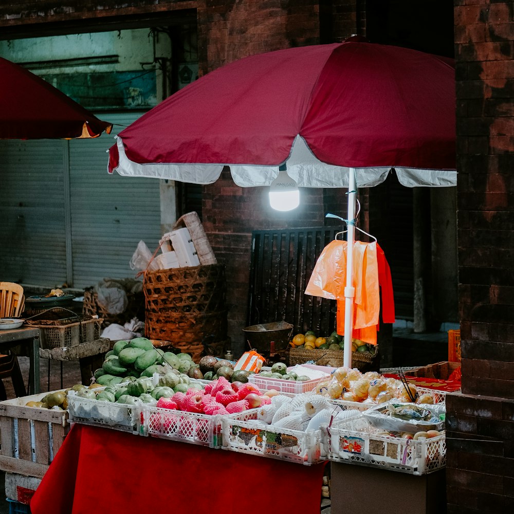 a fruit stand with a red umbrella over it