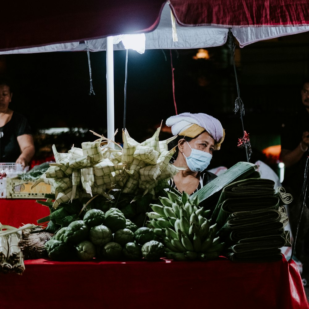 Un hombre con una máscara facial parado frente a un puesto de frutas