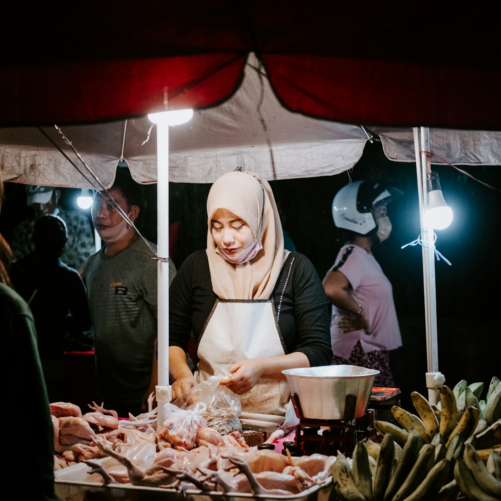 a woman in a headscarf is preparing food at an outdoor market