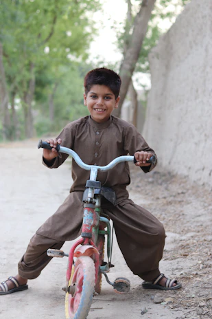 A joyful toddler riding a bright orange Tinywheelz balance bike on a sunny park path.