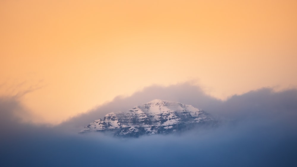 a snow covered mountain in the distance with clouds in the foreground