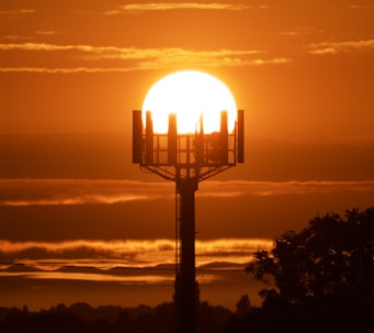 the sun is setting behind a tower with a cell phone on it