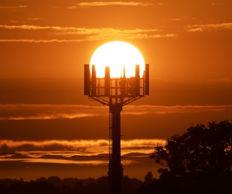 the sun is setting behind a tower with a cell phone on it