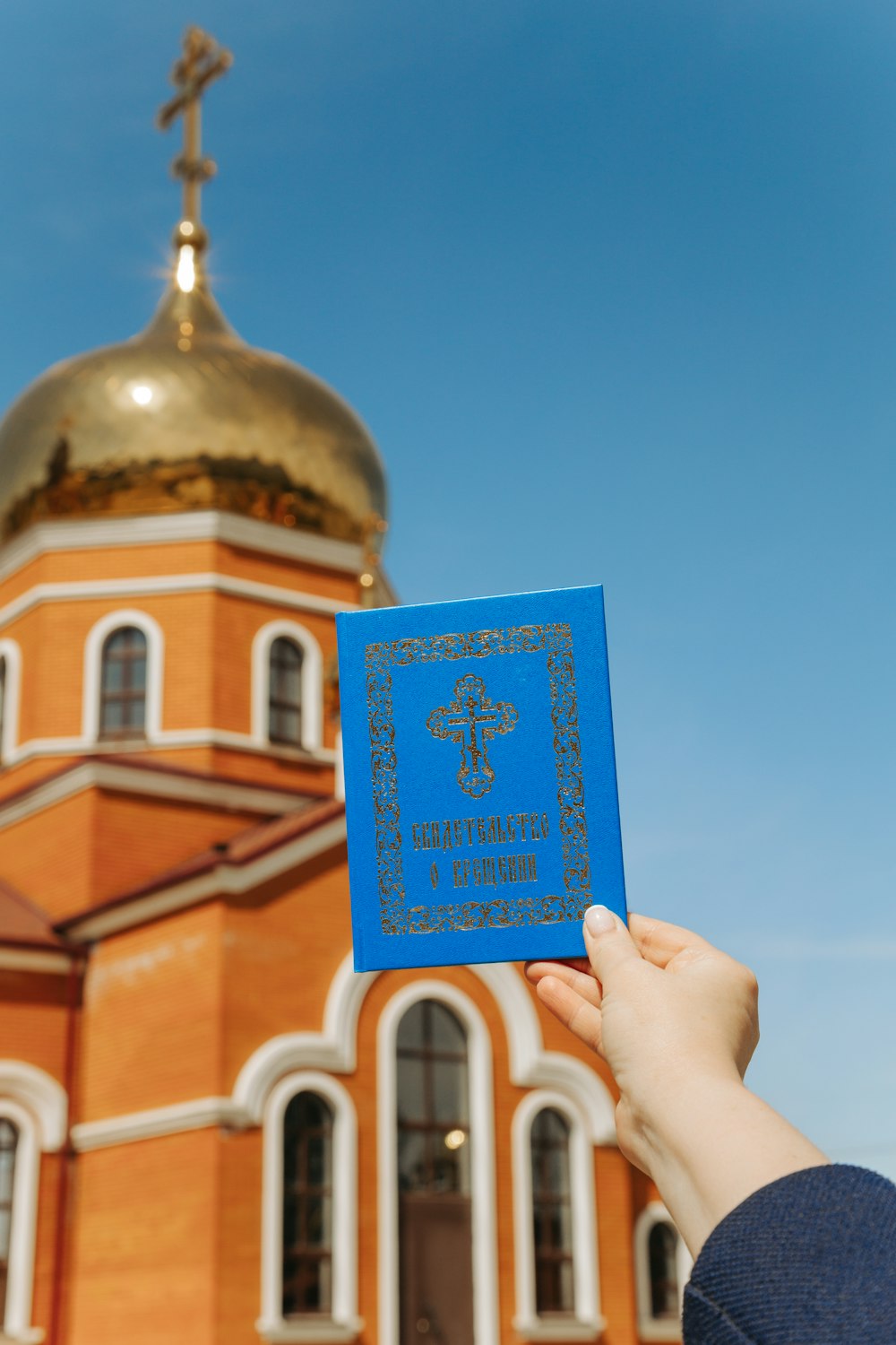 a person holding up a blue book in front of a church